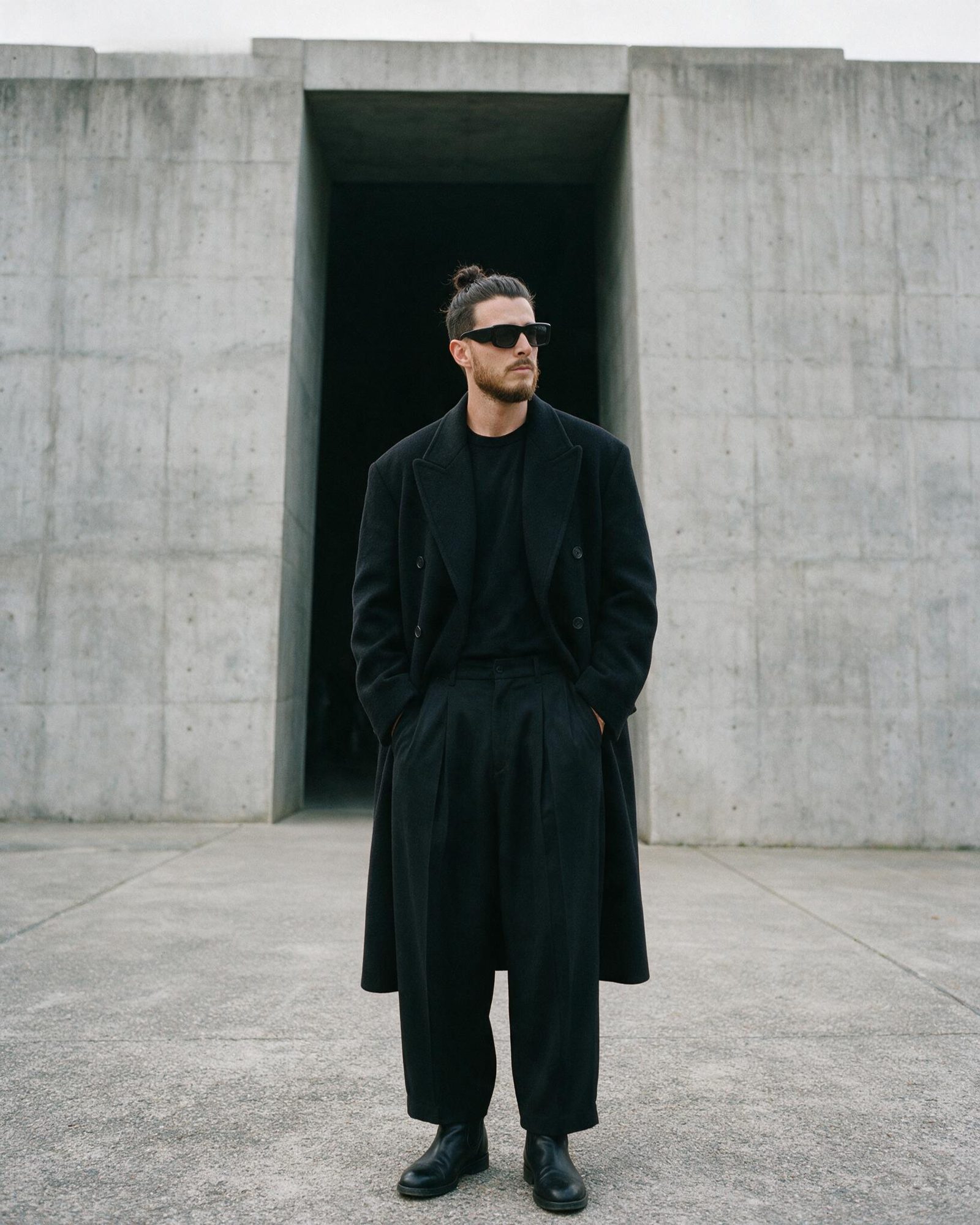 Xavier Roca in a long black coat in front of a dark concrete doorway