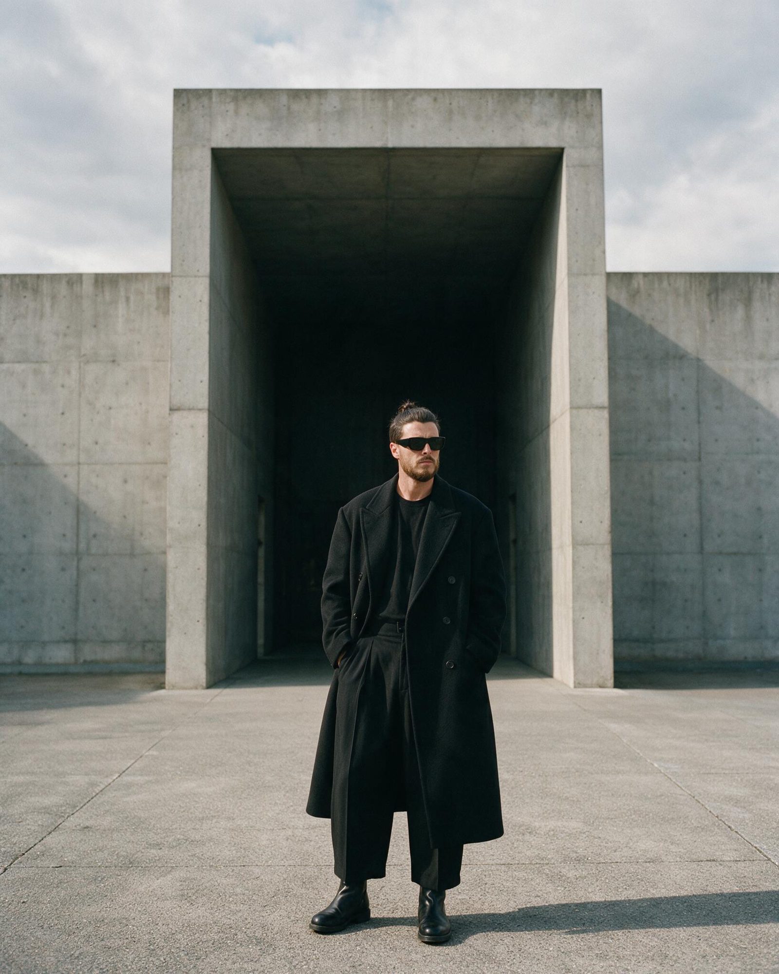 Xavier Roca in a long black coat, standing in front of a concrete entrance